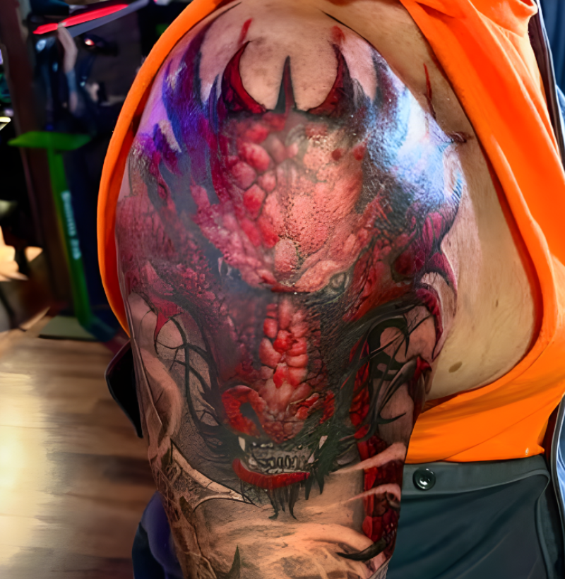 Vibrant red dragon shoulder tattoo with realistic detailing and black shading, created by Bullet’s Ink tattoo artists in Mt Airy, Maryland.