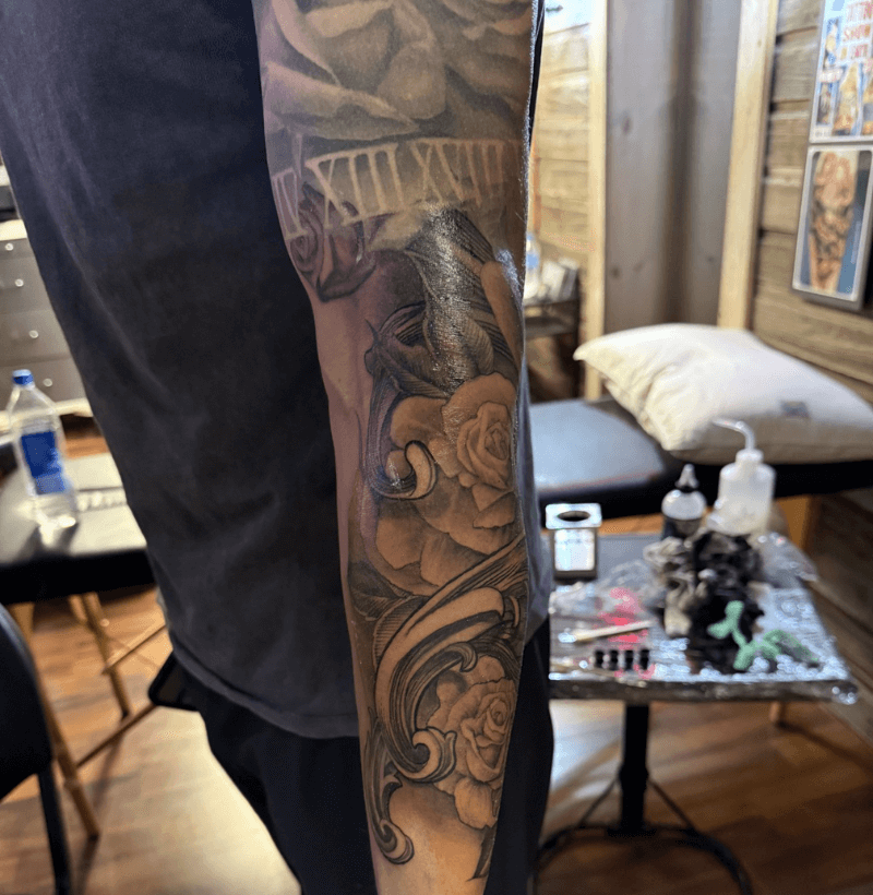 Black and gray sleeve tattoo featuring roses, a clock with Roman numerals, and intricate shading, created at Bullett’s Ink in Mount Airy, Maryland.