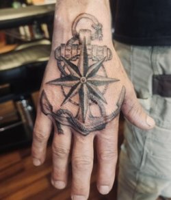 Detailed blackwork compass tattoo on the top of a hand with fine line shading.